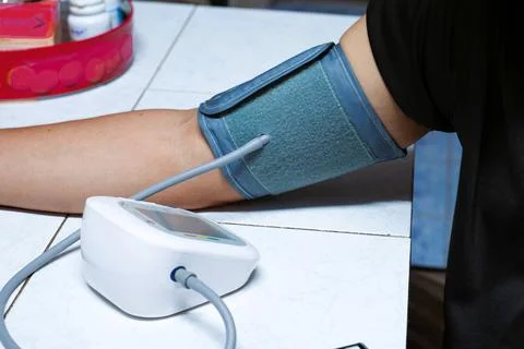 A gray cuff wraps around his arm from a blood pressure monitor. Stock Photos