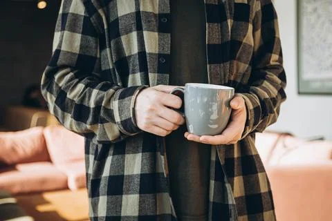 A gray cup in the hands of a man in a checkered shirt in a modern office. Stock Photos