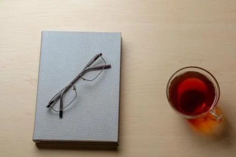 Gray diary, cup of tea, and glasses on a brown table, top view. Stock Photos