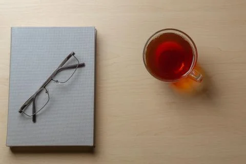 Gray diary, cup of tea, and glasses on a brown table, top view. Copy space Stock Photos