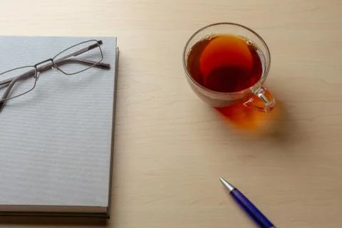 Gray diary, cup of tea, blue pen and glasses on a brown table, selective focu Stock Photos