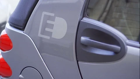 Gray electric car with power socket sign on side. Electro car standing on street Stock Footage 80697656