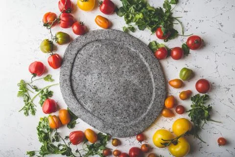 Gray empty stone plate and fresh cooking ingredients - green. red, yellow orange Stock Photos