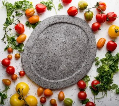 Gray empty stone plate and fresh cooking ingredients - green. red, yellow orange Stock Photos