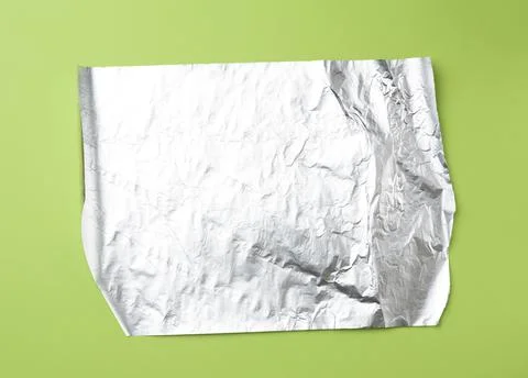 Gray foil for baking and packaging food on a green background, top view Stock Photos