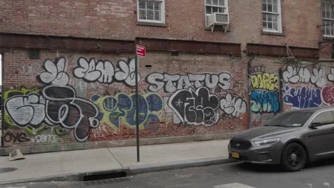 A gray Ford Taurus sits in front of a red brick wall of graffiti Stock Footage 241498805