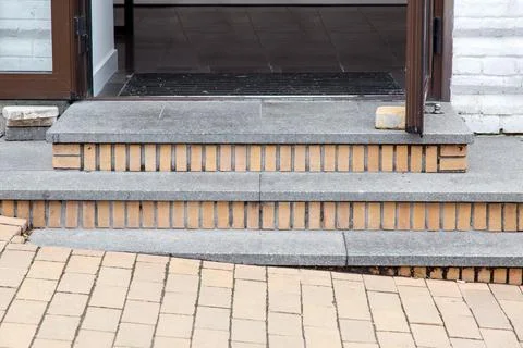 Gray granite steps of a brick threshold at the open entrance door. Stock Photos