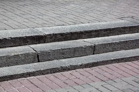Gray granite steps in the middle of stone tile street pavement. Stock Photos