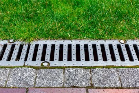 Gray grating of the drainage system for drainage of rainwater in the park. Stock Photos