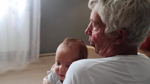 Gray haired calm pensive man looking away while rocking newborn child in his Vídeos de archivo 291306138