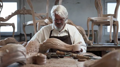 Gray-haired Carpenter leads hands and looking carving wooden detail Furniture Stock Footage 112627804