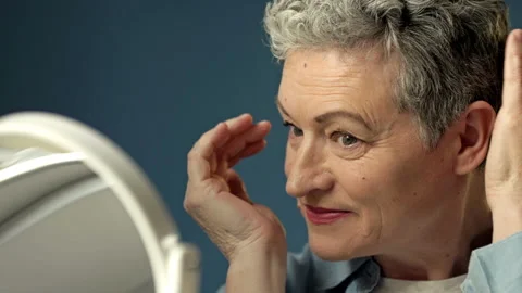 Gray-haired elderly woman straightens her hair in front of a mirror before Stock Footage 172396653