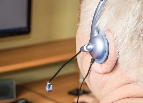 A gray-haired fat old man with a headset looks at the monitor screen, remote  Foto stock