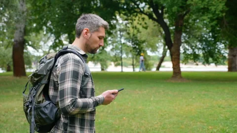 Gray-haired focused man travel blogger walks park using gps maps in smartphone Video stock 136824183