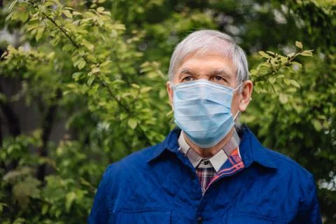 Gray-haired grandfather with covid protection on face with green background. Old Stock Photos