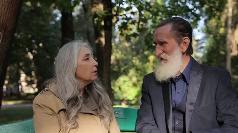 Gray-haired grandmother and old pensioner talking while sitting on a bench in a Stock Footage 323915347