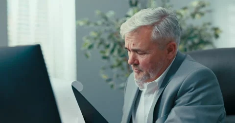 The gray-haired head of the company sits at desk in comfortable chair of the Stock Footage 164873404