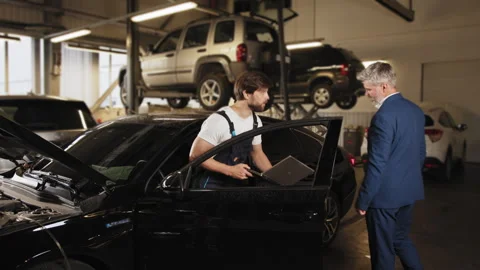 Gray-haired male client communicates with an electrician in a car service. Auto Stock Footage 243364836