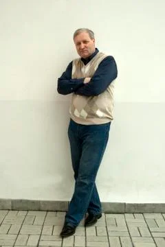 A gray-haired man of 50 years stands cross-legged Stock Photos