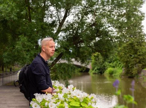 Gray-haired man with a backpack leaning on a fence near the river Foto stock