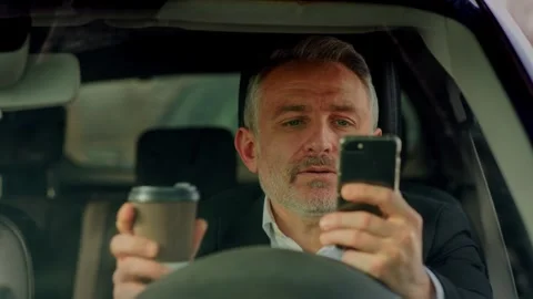 A gray-haired man with a beard sits in a car and drinks coffee. A man in a Stock Footage 242605089