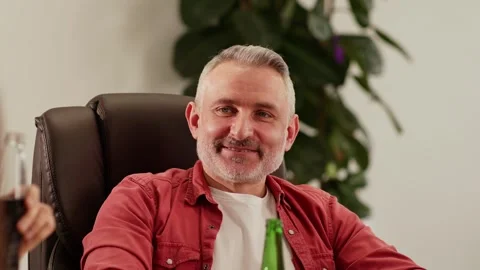 A gray-haired man with a beard sits in a chair and talks to his colleagues Stock Footage 243366695