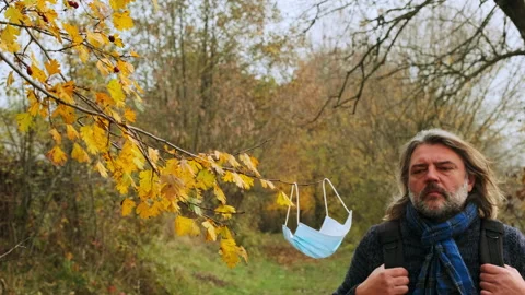Gray-haired man with a beard wears a medical mask in the forest in autumn Stock Footage 146749378