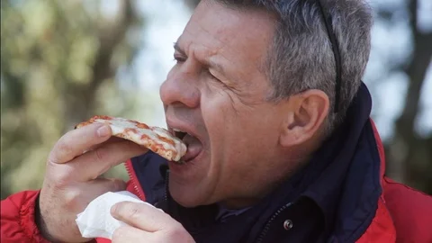Gray-haired man with a big appetite eating a piece of pizza on the street Video stock 100943206