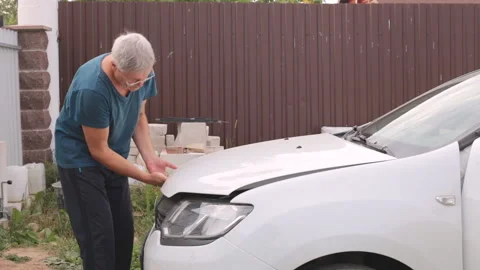 The gray-haired man cannot open the hood of the car. The hood is jammed and the Video stock 237750057
