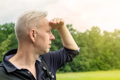 The gray-haired man, closing his eyes with his hand from the sun, looks Stock Photos