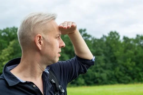 The gray-haired man, closing his eyes with his hand from the sun, looks Stock Photos