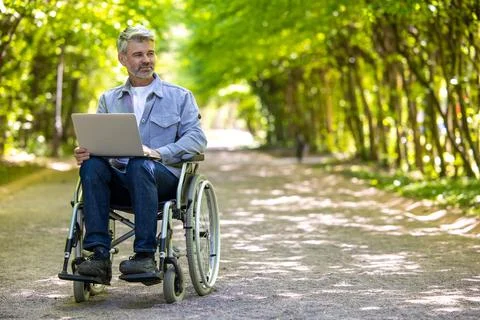 Gray haired man freelancer with disability in wheelchair working online. Stock Photos