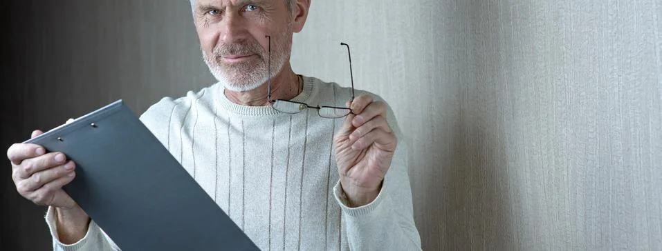 Gray-haired man in light clothes and glasses enters into a contract on paper Stock Photos