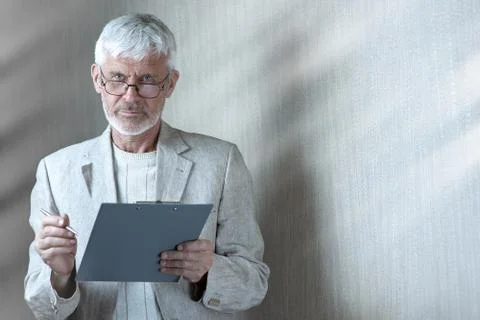 Gray-haired man in light clothes and glasses enters into a contract on paper 写真素材