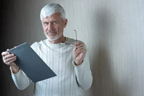 Gray-haired man in light clothes and glasses enters into a contract on paper 库存照片