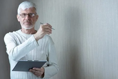 Gray-haired man in light clothes and glasses enters into a contract on paper Stockfoto's