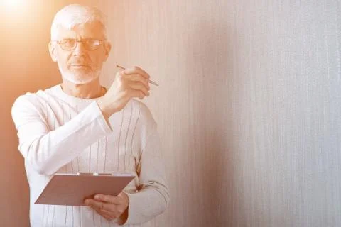 Gray-haired man in light clothes and glasses enters into a contract on paper Stockfoto's