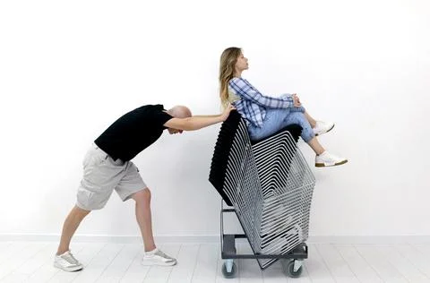 A gray-haired man pushes a stack metal chairs on which a young woman is sitting. Stock Photos