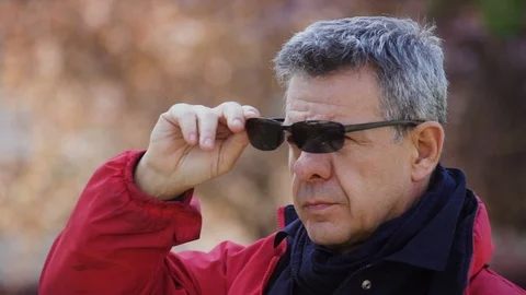 A gray-haired Man in a red jacket takes off his sunglasses and looks around Stock Footage 100945827