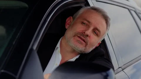 A gray-haired man sits in a car and looks away. A man in a business suit stuck Stock Footage 242609567