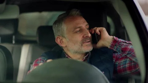 A gray-haired man sits in a car and talks on the phone. Smiling bearded man Stock Footage 242610580