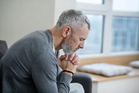 A gray-haired man sitting with eyes closed and saying the payers Stock Photos