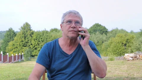A gray-haired man smokes a cigarette and talks on a mobile phone. Adult man with Stock Footage 237749252