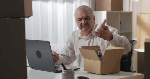 Gray-haired man in a white shirt checks an order to be sent to a customer using Stock Footage 149471739