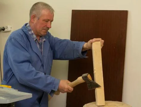 A gray-haired man in work clothes works with an axe. chops the log. carpenter's Stock Photos