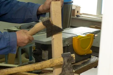 A gray-haired man in work clothes works with an axe. chops the log. carpenter's Stock Photos