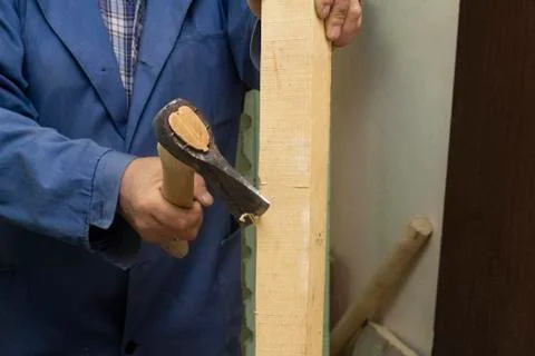A gray-haired man in work clothes works with an axe. chops the log. carpenter's Stock Photos