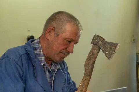 A gray-haired man in work clothes works with an axe. chops the log. carpenter's Stock Photos