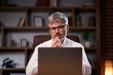 Gray-haired manager in glasses uses a laptop, conducts a video conference in the Stock Photos