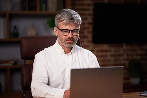 Gray-haired manager in glasses uses a laptop, conducts a video conference in the Foto stock